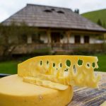 Roată de cașcaval cu felii găurite, lângă casă tradițională