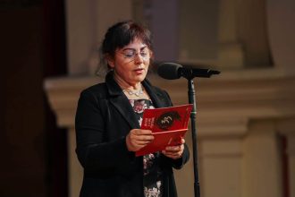 Femeie citește dintr-o broșură roșie la microfon