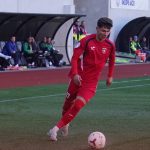 Fotbalist în echipament roșu conduce mingea pe teren
