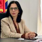 Femeie la birou, lângă microfon și drapele