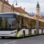 Autobuz articulat pe stradă istorică, cu munți în fundal