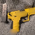 Pistol galben cu încărcător metalic pe covor gri