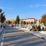 Alee asfaltată într-un cimitir cu cruci și monumente funerare