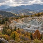 Carieră montană cu excavator, înconjurată de pădure tomnatică