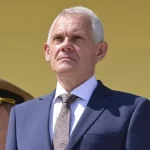 Bărbat în costum, flancat de doi militari