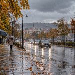 Pietoni cu umbrele pe stradă ploioasă de toamnă