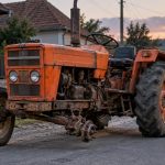 Tractor portocaliu vechi pe stradă rurală la apus
